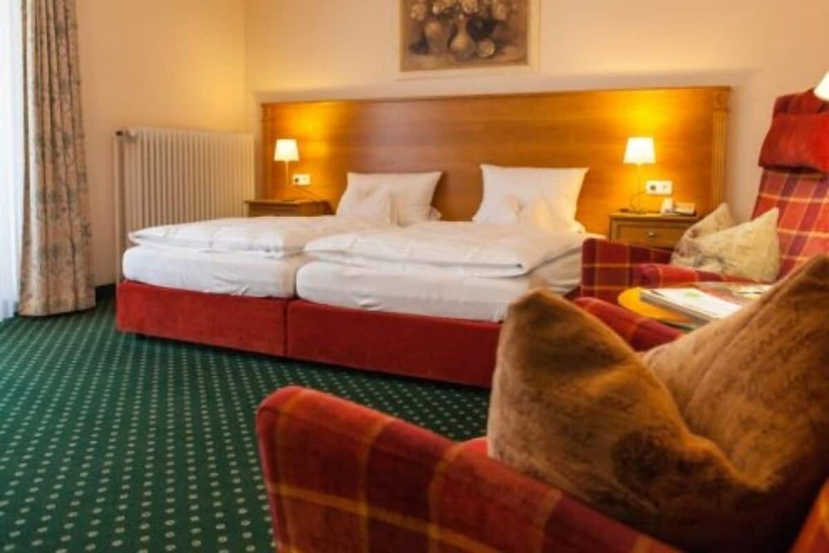 A hotel room with a double bed, two bedside tables with lamps, a red sofa, and a painting on the wall.