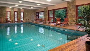 Une piscine intérieure dotée d’un sol carrelé, de murs en pierre et de chaises longues en bois.