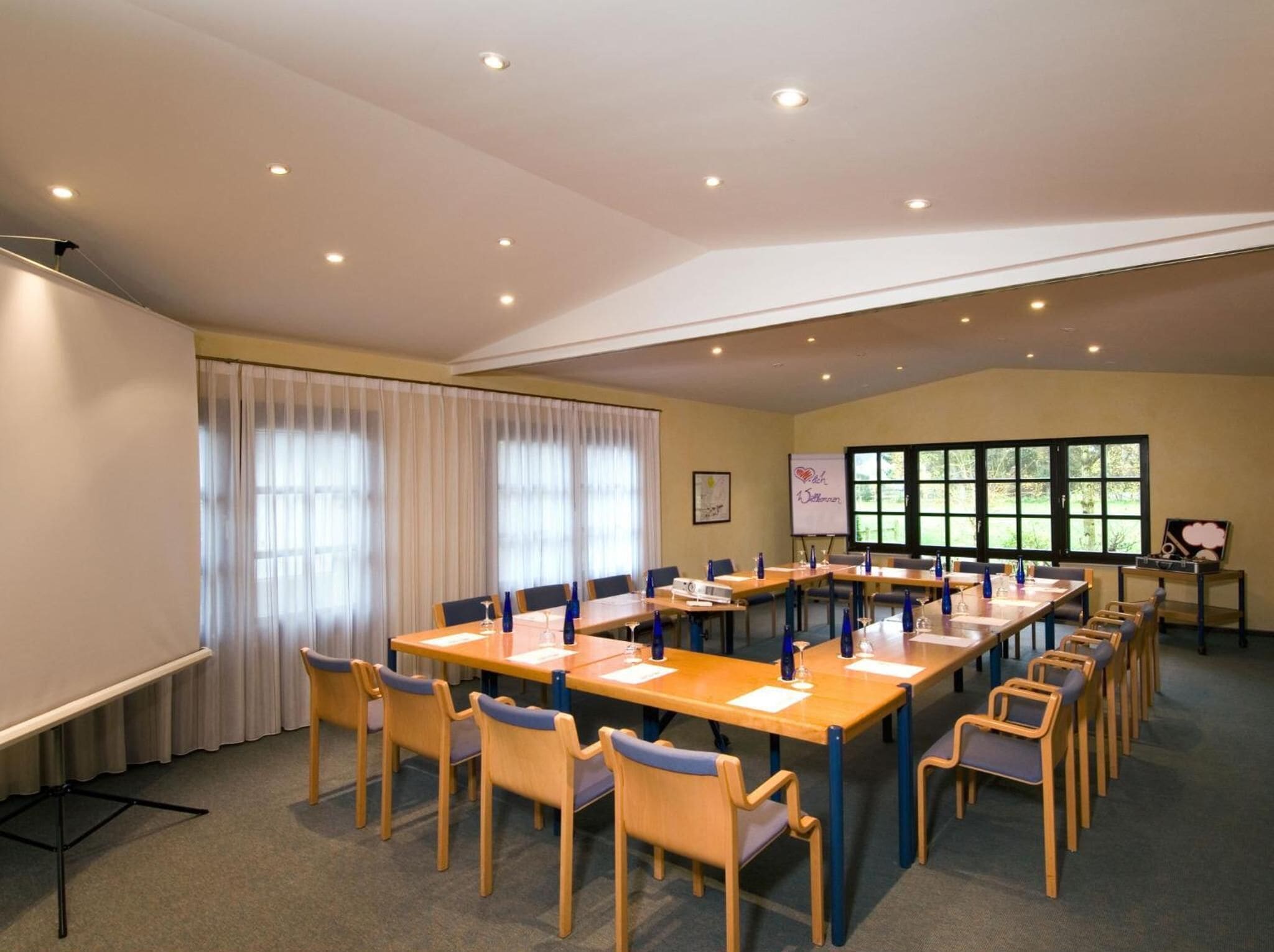 Ein Konferenzraum mit langem Tisch, Stühlen, einer Whiteboard und einer Projektionsfläche.