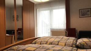 A hotel room with a bed, a wardrobe, a chair, and a window with curtains. - Ferienwohnungen Domizil (Bad Bertrich)