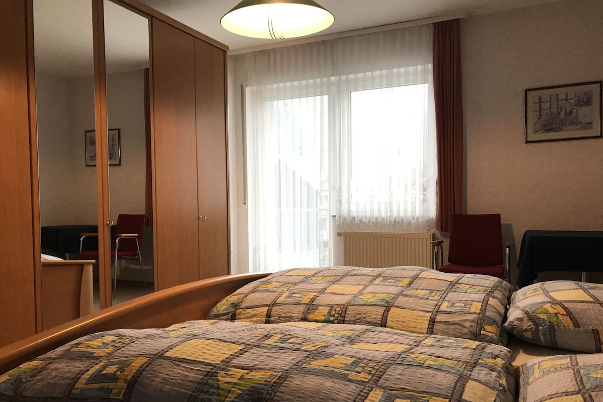 Une chambre d’hôtel avec un lit, une armoire, une chaise et une fenêtre avec des rideaux.