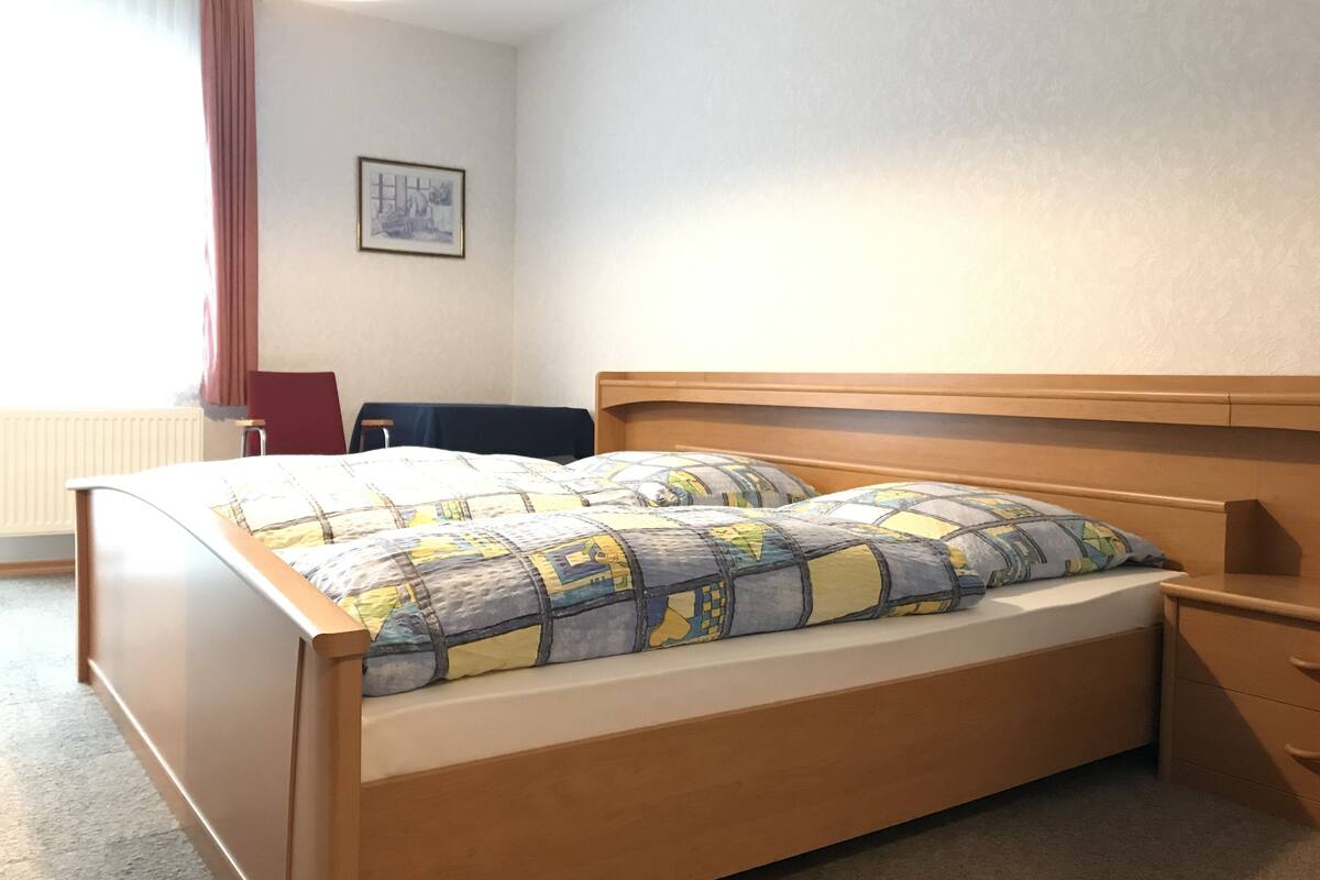 Un lit simple avec une tête de lit en bois, une table de chevet et un tableau accroché au mur.