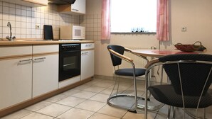 A kitchen with white cabinets, a microwave, an oven, a sink, and a window with pink curtains. - Ferienwohnungen Domizil (Bad Bertrich)