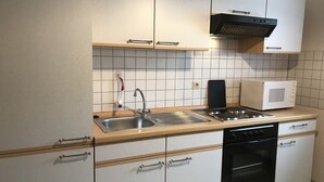 A compact kitchen with a sink, stove, microwave, and oven. - Ferienwohnungen Domizil (Bad Bertrich)