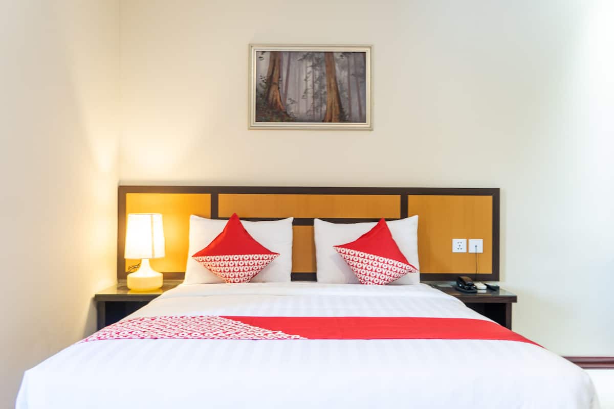 A hotel room with a large bed, two red and white patterned pillows, a bedside lamp, and a framed picture on the wall.