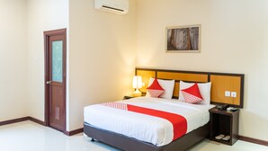 Een hotelkamer met een bed, nachtkastje, airconditioning en een schilderij aan de muur.