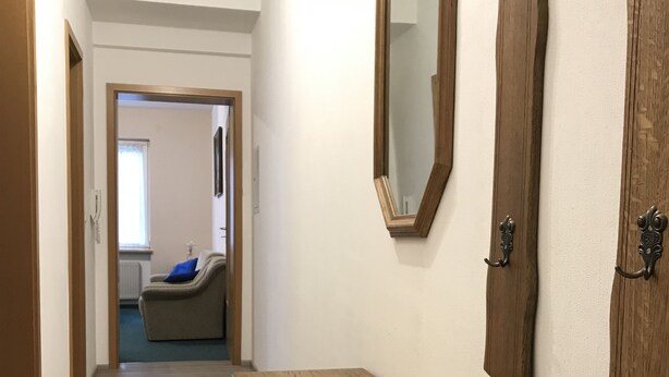 Un couloir avec un banc en bois, un miroir et une porte.