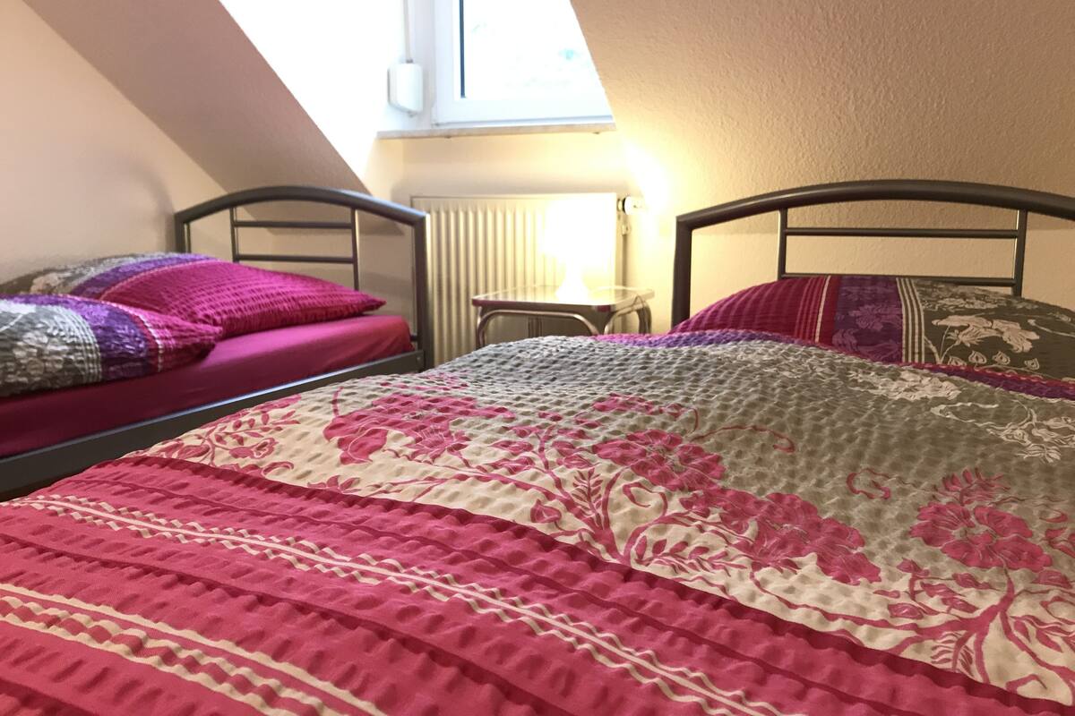 Un dormitorio con dos camas, una mesita y una ventana que deja entrar luz natural.