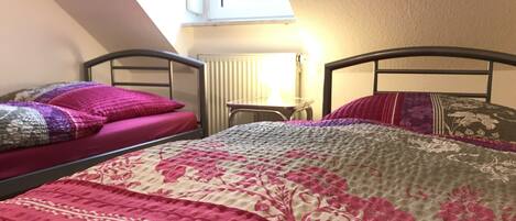 A dormitory room with two beds, a small table, and a window providing natural light.