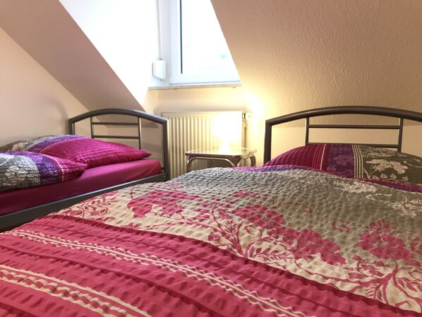 A dormitory room with two beds, a small table, and a window providing natural light.
