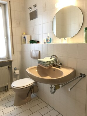 A bathroom with a toilet, sink, and mirror. There is a towel rack with folded towels, a soap dispenser, and a bottle of hand soap on the sink.