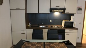 Une cuisine compacte équipée d’un four à micro-ondes, d’une cuisinière et d’un évier. On y trouve deux chaises noires et une table recouverte d’un set de table en fibres tressées.
