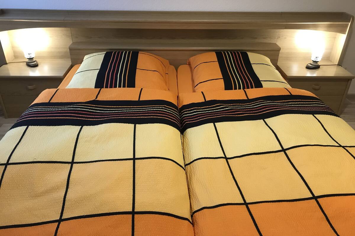 Una cama doble con una colcha a rayas y dos lámparas de noche sobre mesitas de madera.