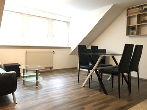 A modern living room with a glass table and black chairs, a radiator, and a large window.