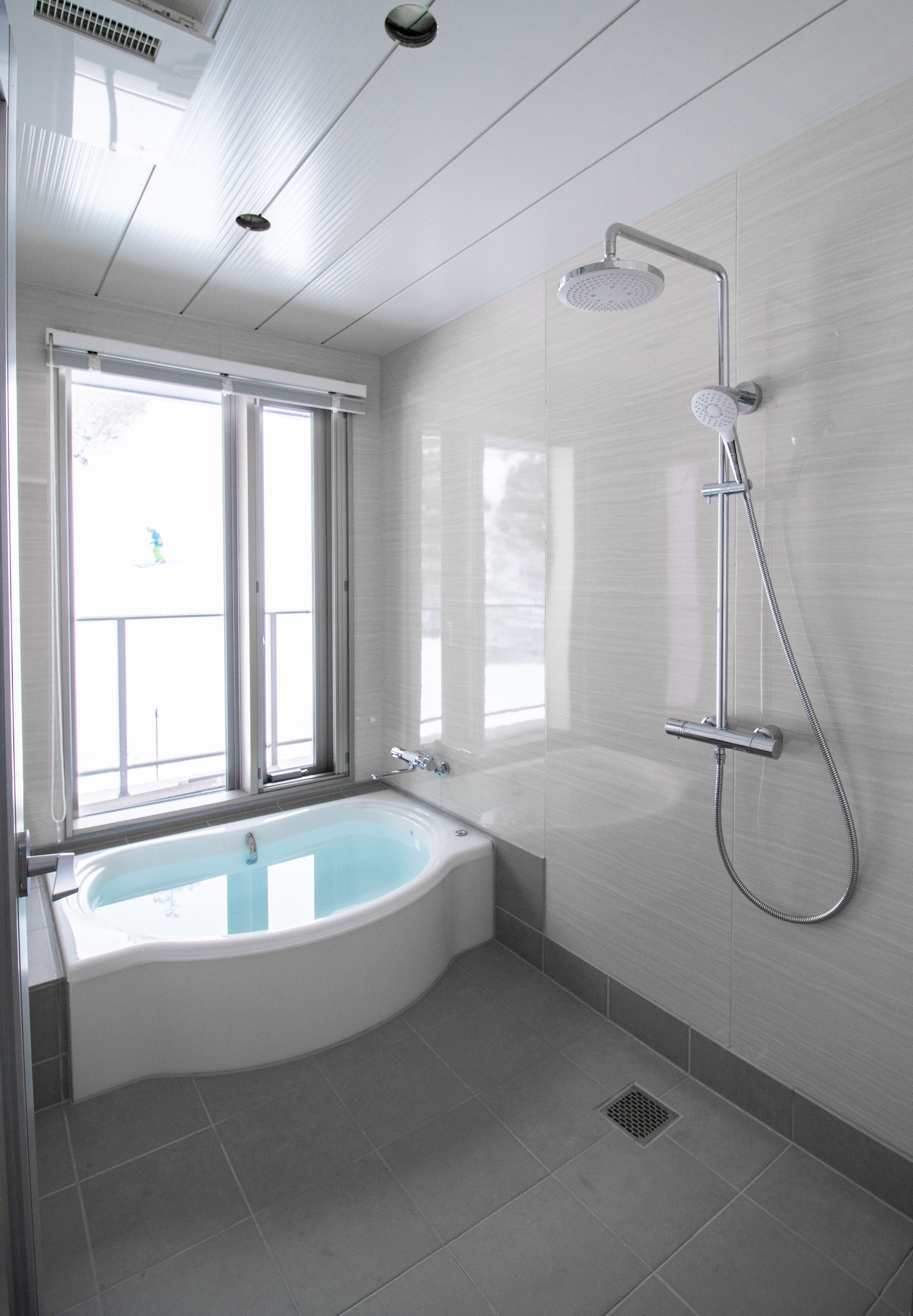 A modern bathroom with a freestanding bathtub, a showerhead, and a window providing natural light.