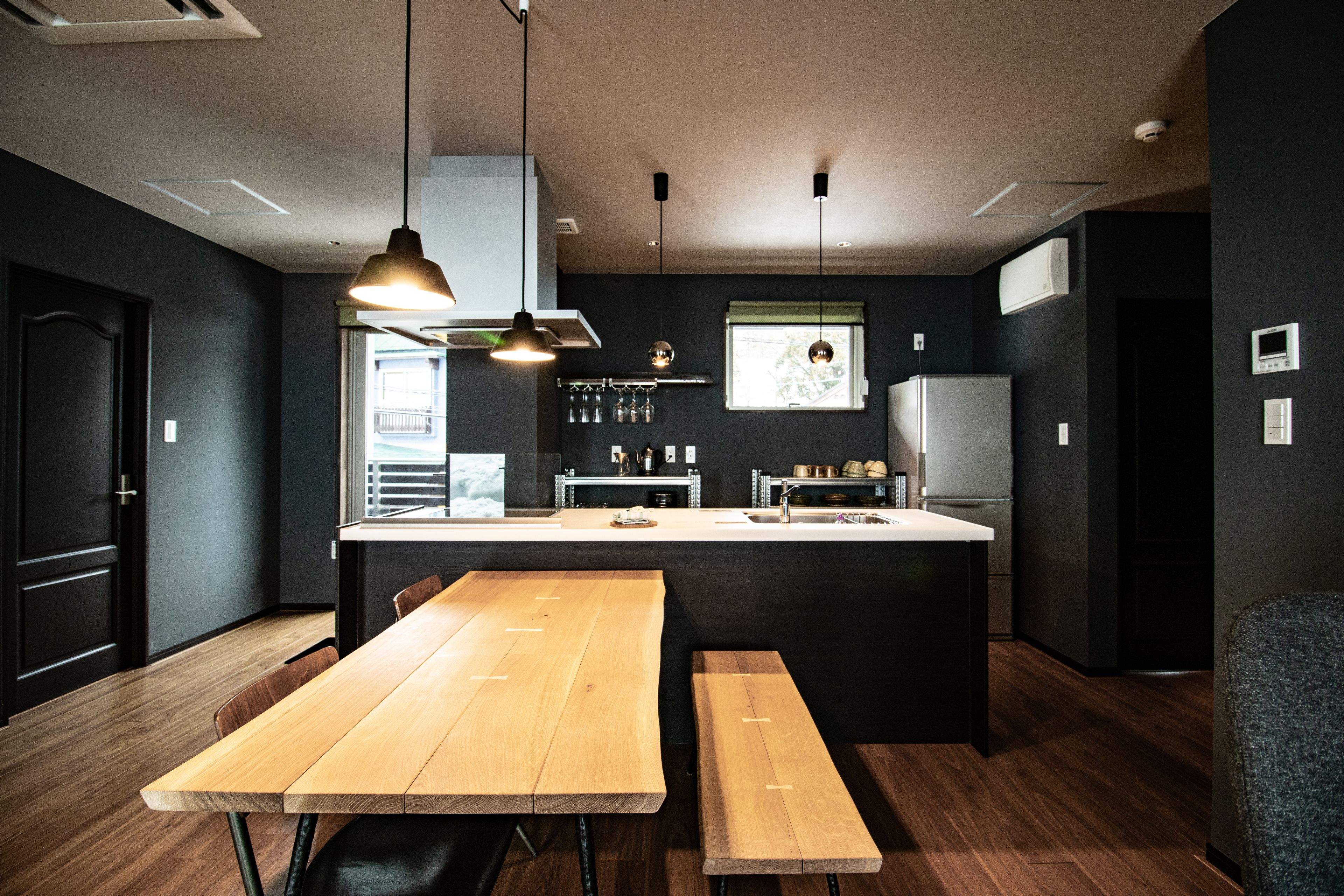A modern kitchen with a central island, wooden benches, pendant lighting, and a view of the outdoors.