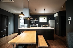 A modern kitchen with a central island, wooden benches, pendant lighting, and a view of the outdoors.