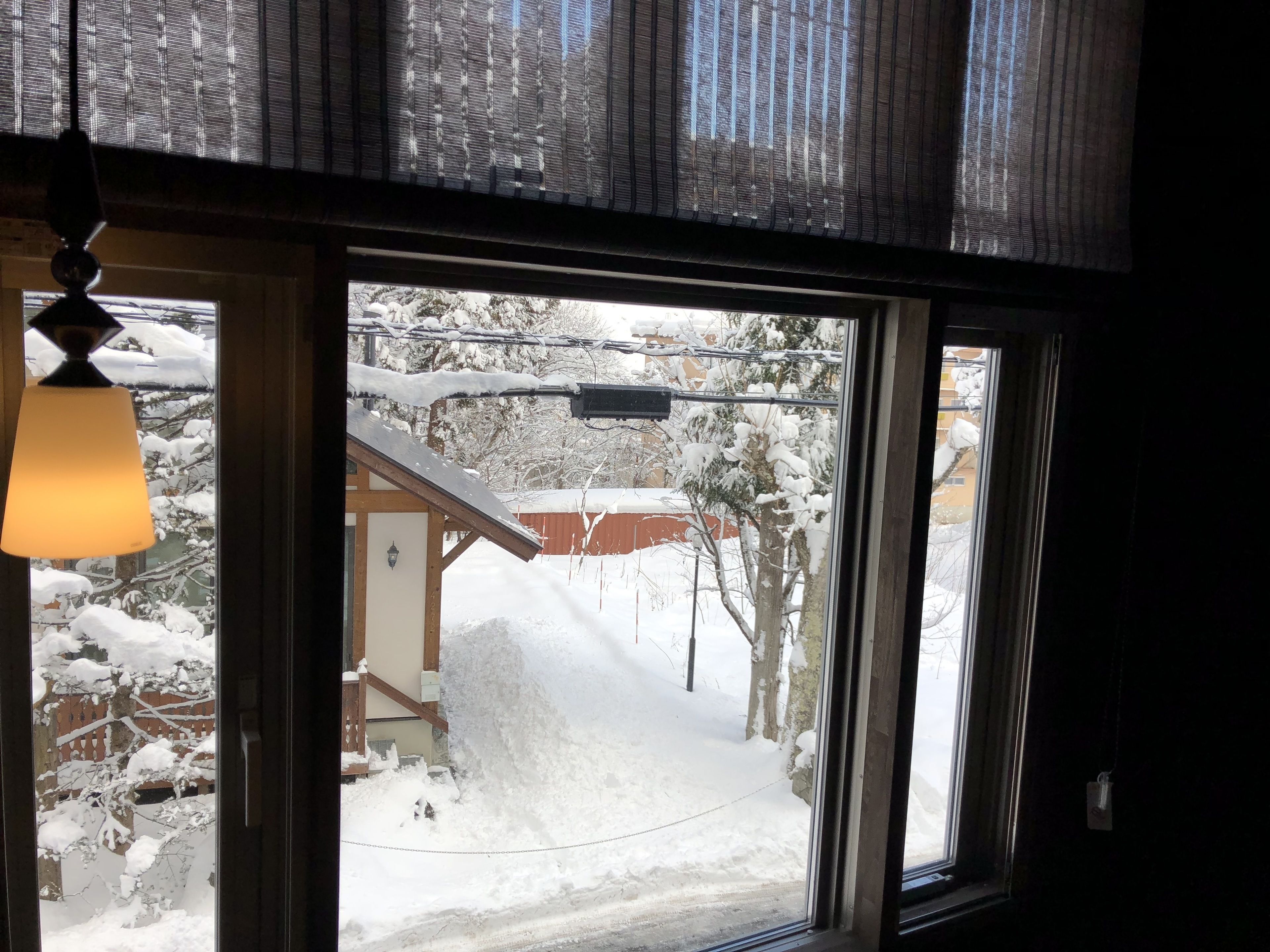 A view through a window with a snow-covered landscape, a building with a red roof, and a hanging lamp.