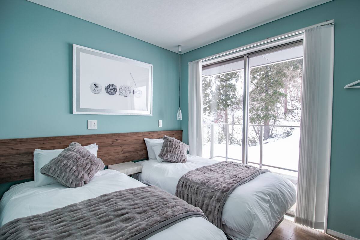 A bedroom with two beds, a large window, and a framed artwork on the wall.