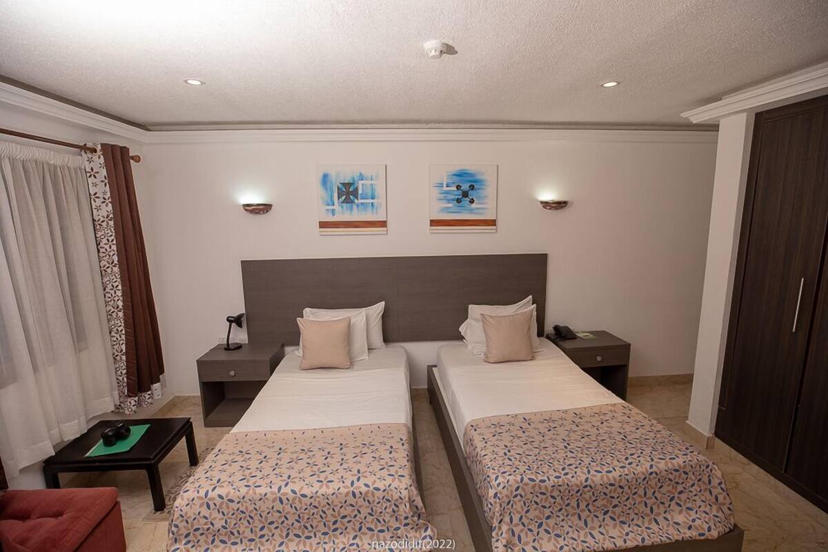 A hotel room with two beds, a desk, a chair, and a wardrobe.