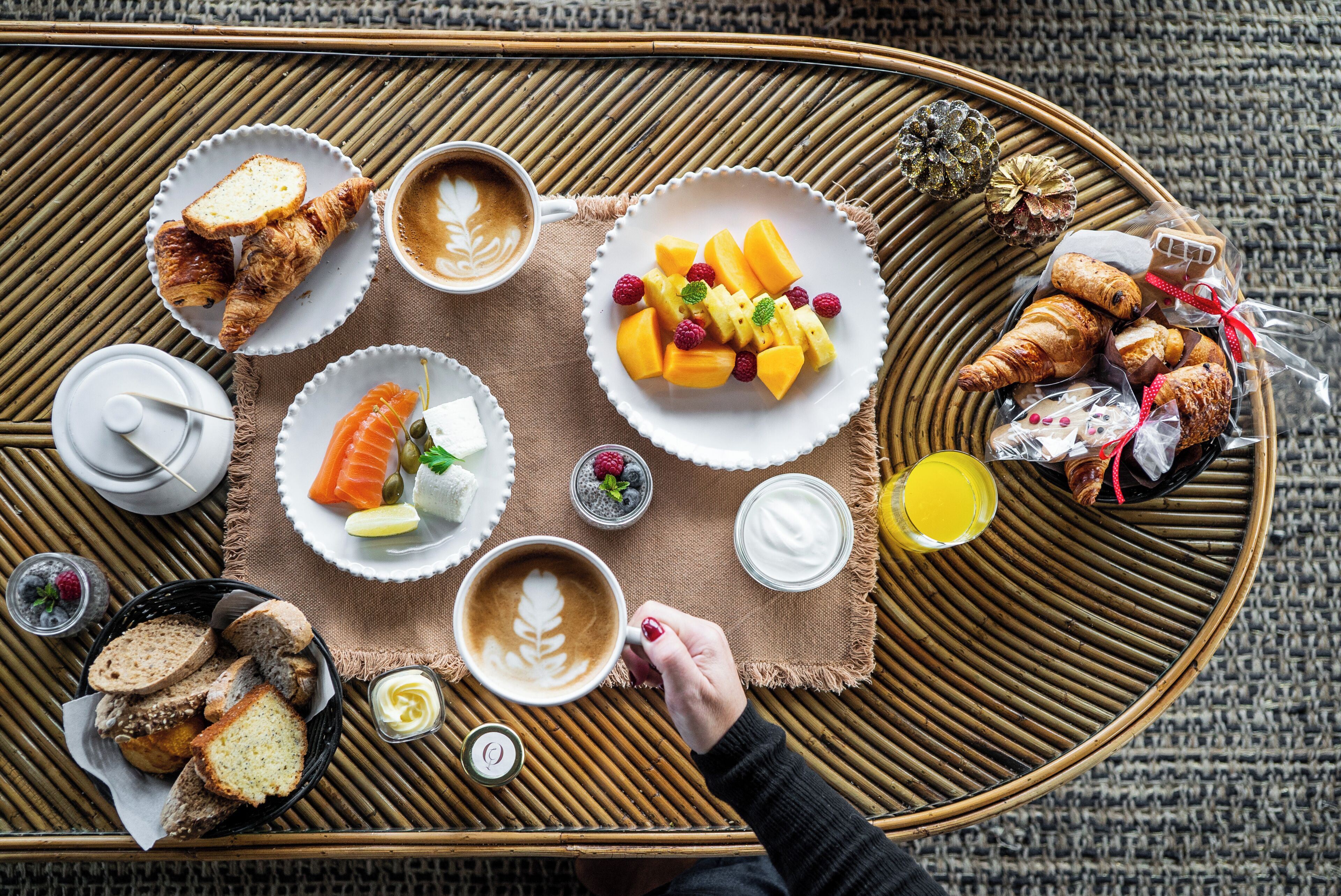A breakfast tray with croissants, fruit, coffee, and pastries on a woven mat.