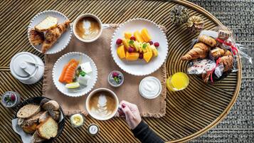 A breakfast tray with croissants, fruit, coffee, and pastries on a woven mat.