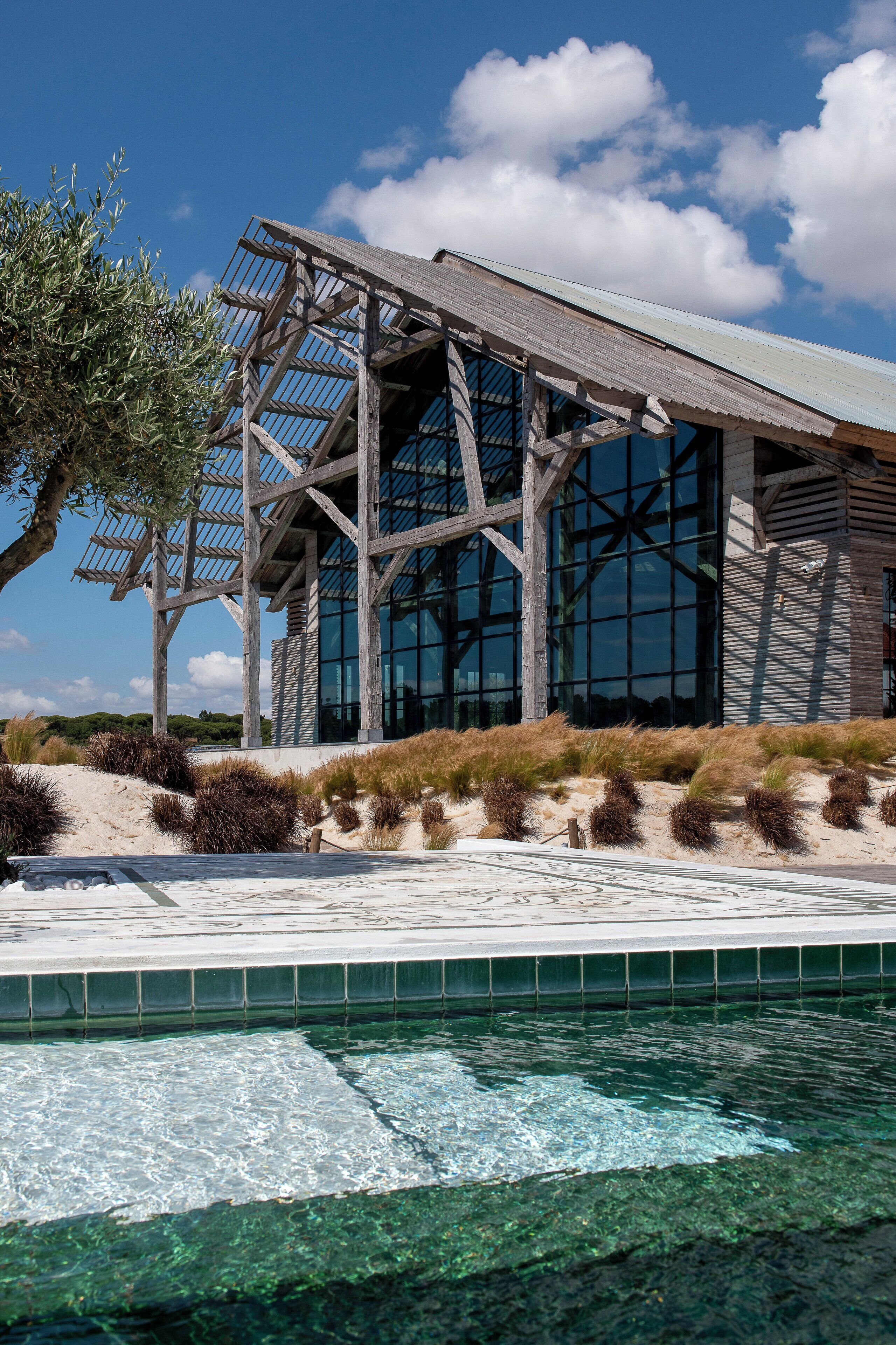 Un bâtiment moderne doté d’une façade en verre et d’une structure en bois, situé à côté d’une piscine.