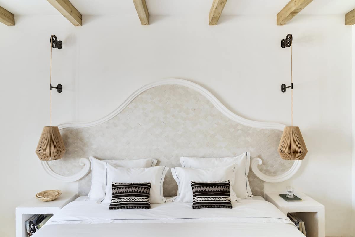 A bed with a white headboard, two bedside tables, and a hanging lamp.