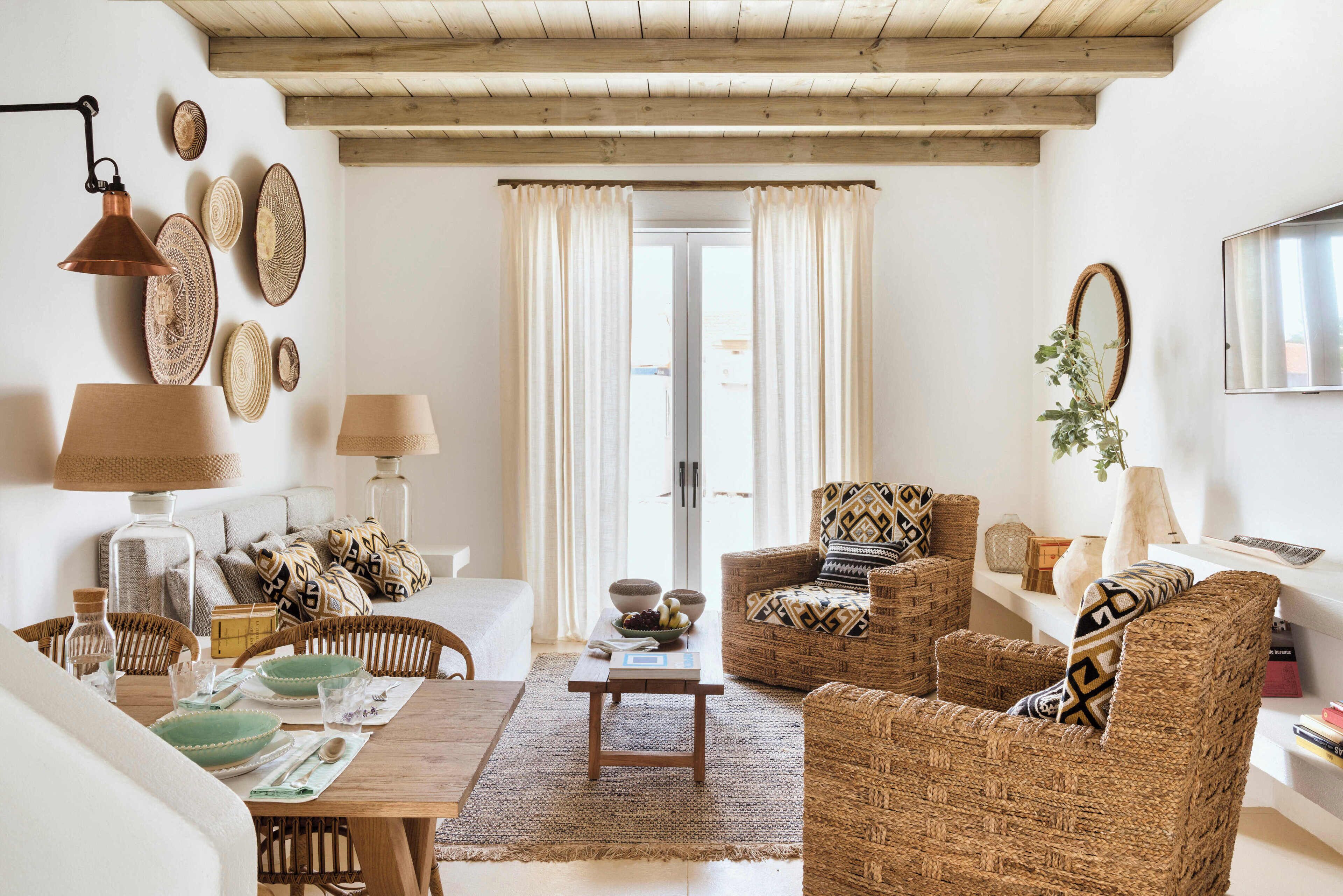 Un salon chaleureux, avec des meubles en osier, un plafond en bois et une vue dégagée sur l’extérieur grâce à une porte vitrée.