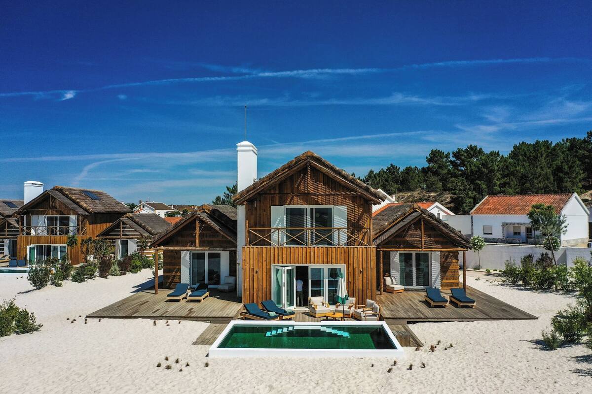 A wooden villa with a pool, multiple balconies, and a beach view.