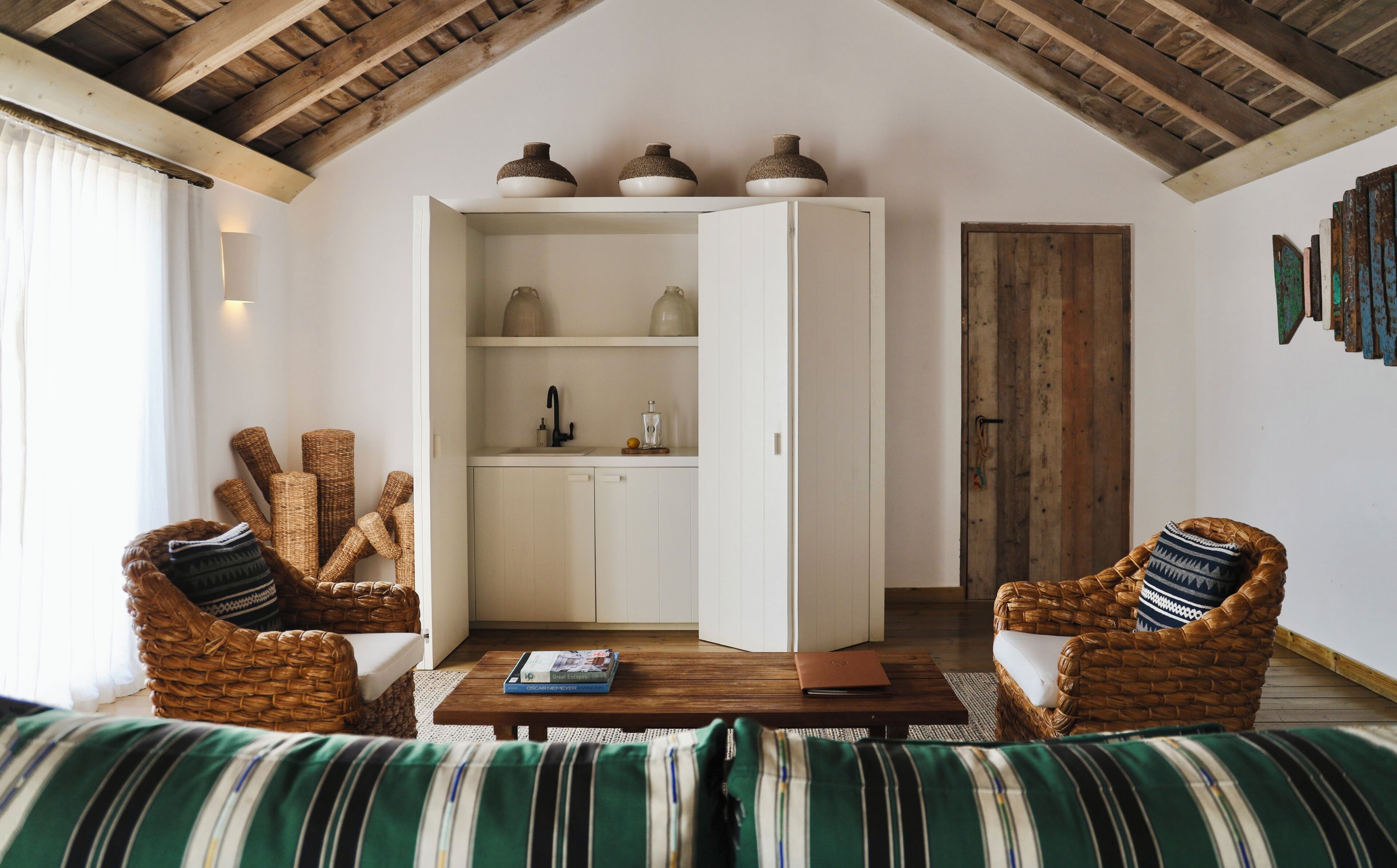 A cozy living room with wicker furniture, a white cabinet, and a wooden ceiling.