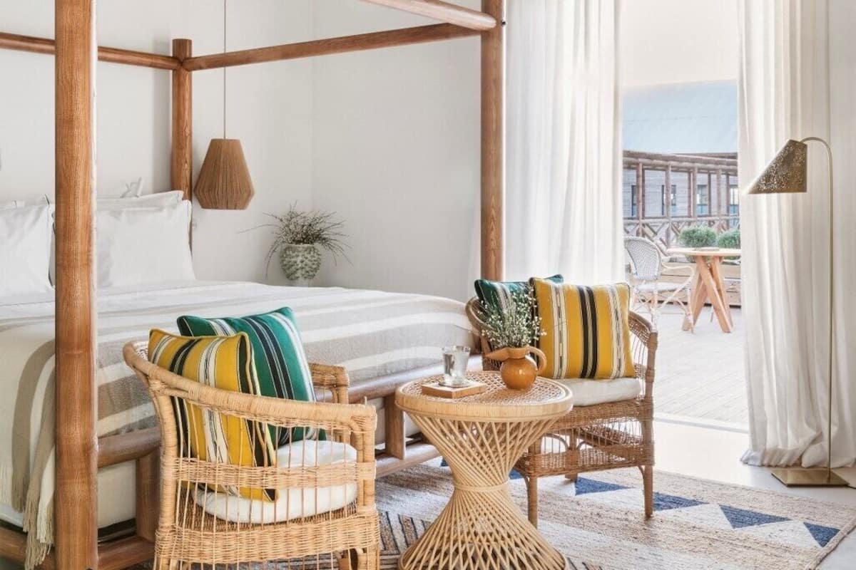 A room with a wooden ceiling, a bed, wicker furniture, and a view of the sea.