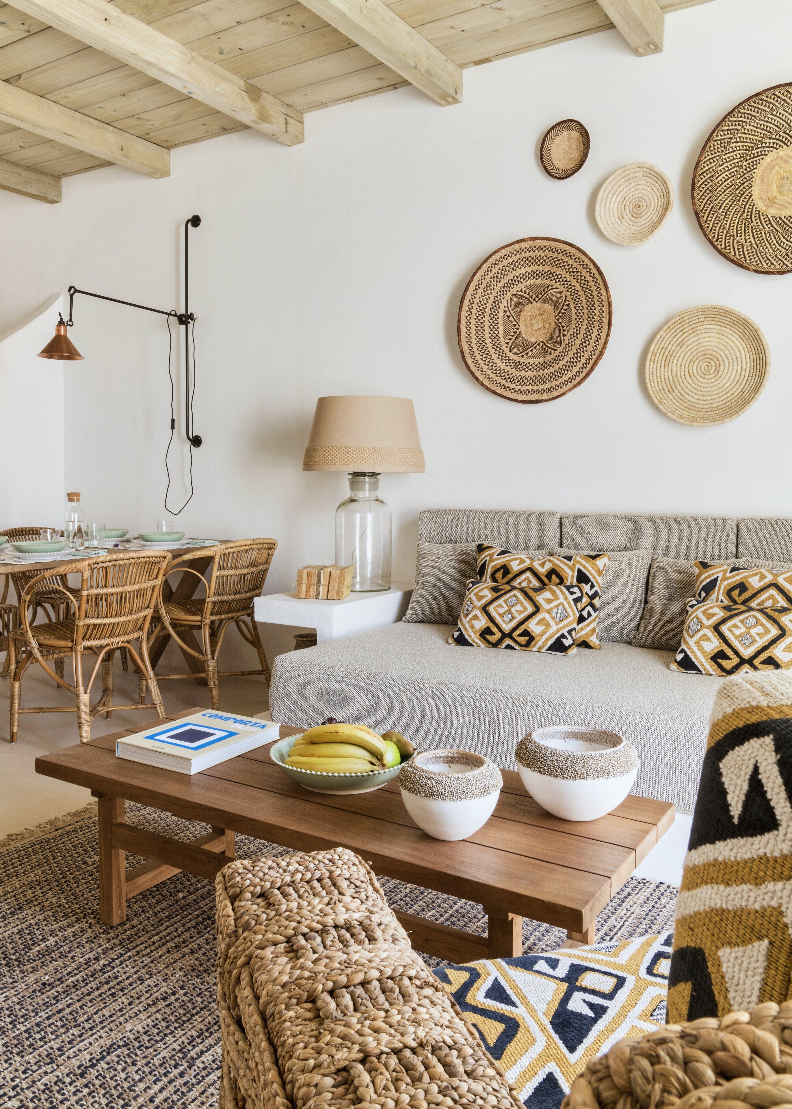 A cozy living room with a wooden ceiling, a dining area with wicker furniture, and a sofa with patterned cushions.