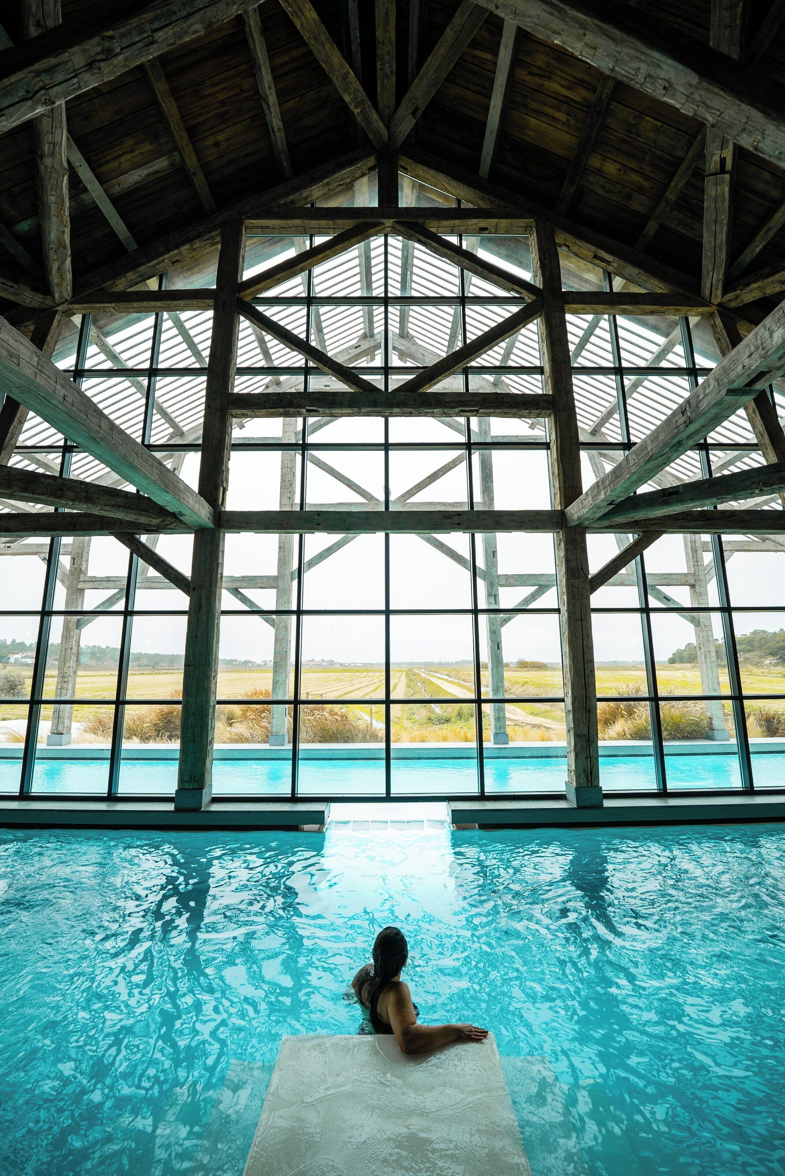 An indoor swimming pool with a view of a field through large windows.