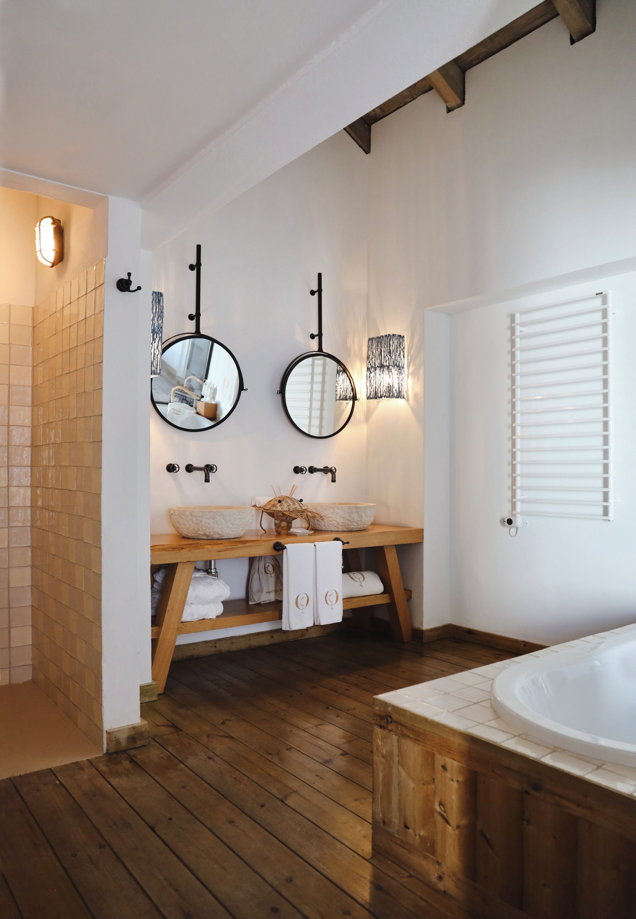 A bathroom with two round mirrors, a wooden vanity, a bathtub, and a tiled floor.