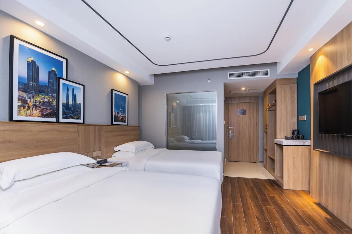 Habitación de hotel con dos camas, televisión, baño y cuadros con vistas a la ciudad.