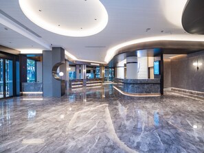 Un vestíbulo moderno con piso de mármol, mostrador de recepción curvo y grandes ventanales con vistas a la ciudad.