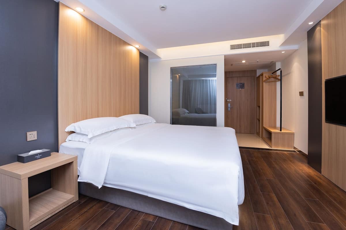 Una habitación de hotel moderna con una cama grande, una mesita de noche, un armario y un televisor.