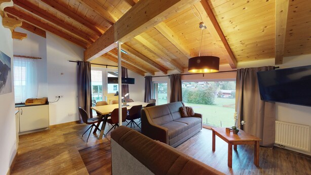 Un salón acogedor con techo de madera, un sofá, un televisor y una zona de comedor con mesa y sillas.