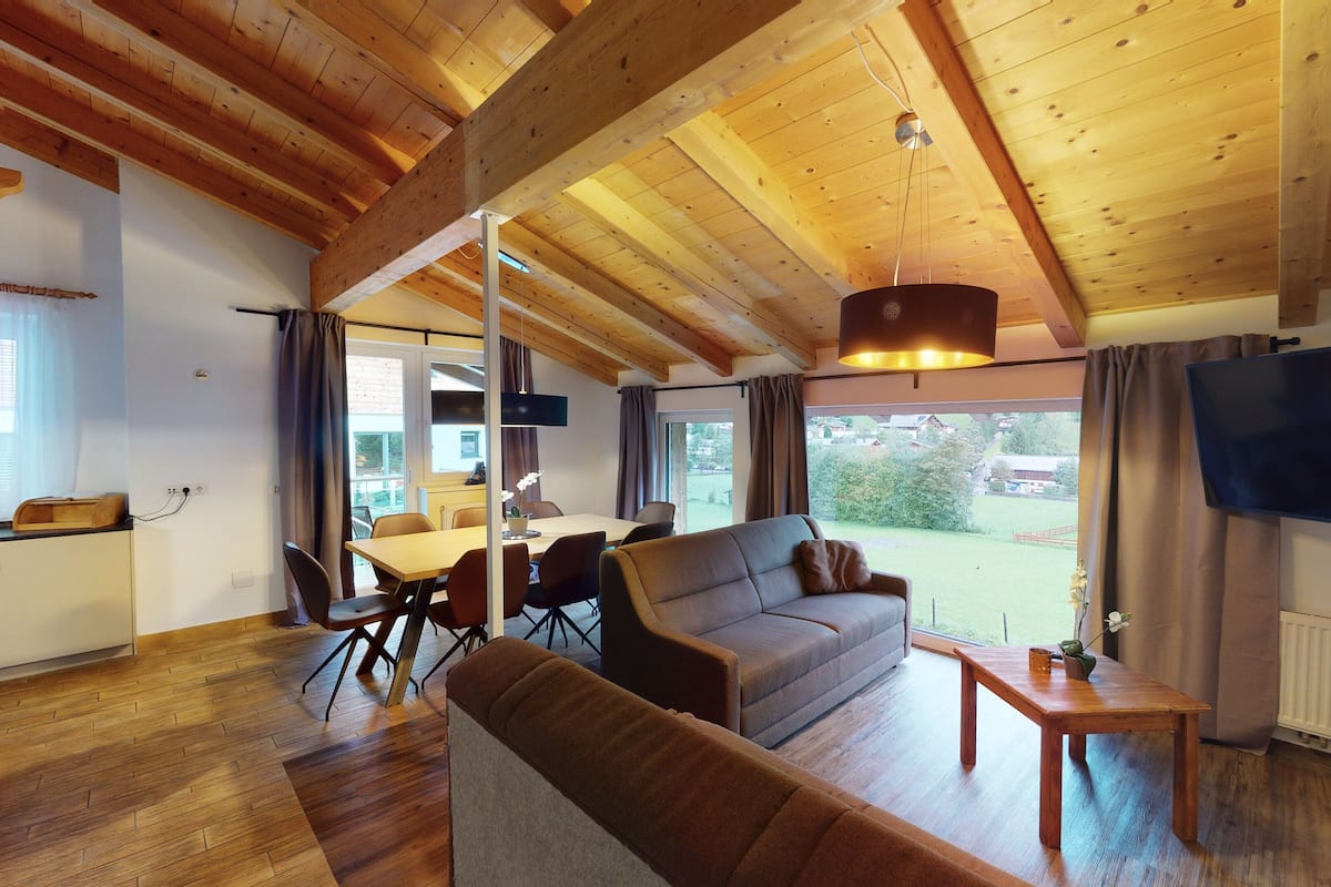 A cozy living room with a wooden ceiling, a sofa, a TV, and a dining area with a table and chairs.