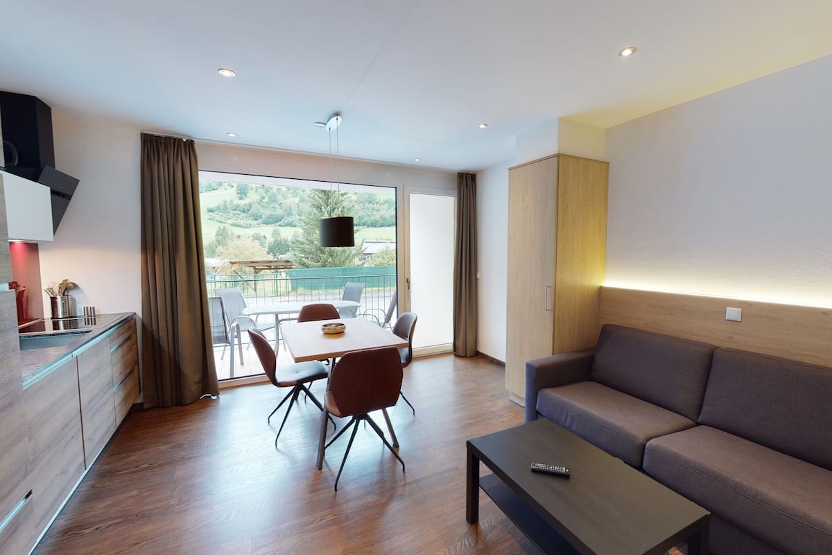 A modern living room with a sofa, a coffee table, and a dining area with chairs and a table.
