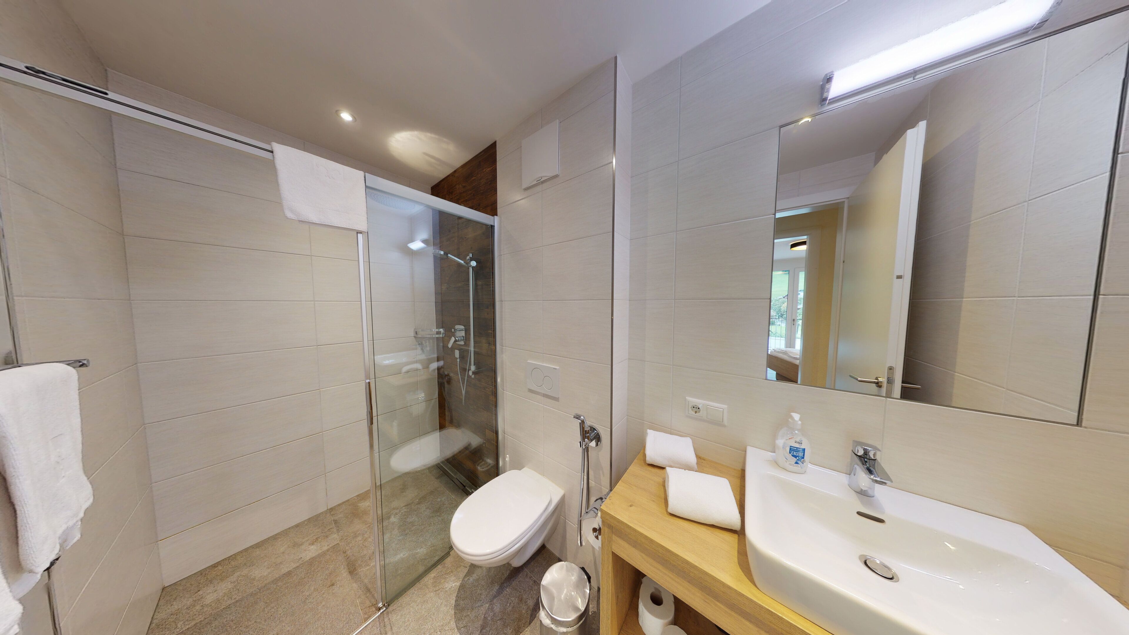 Un baño moderno con cabina de ducha de vidrio, inodoro, lavabo con espejo y toallero.