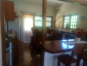 Una cocina con armarios de madera, una mesa de comedor con sillas, un refrigerador y un ventanal con vistas al exterior.