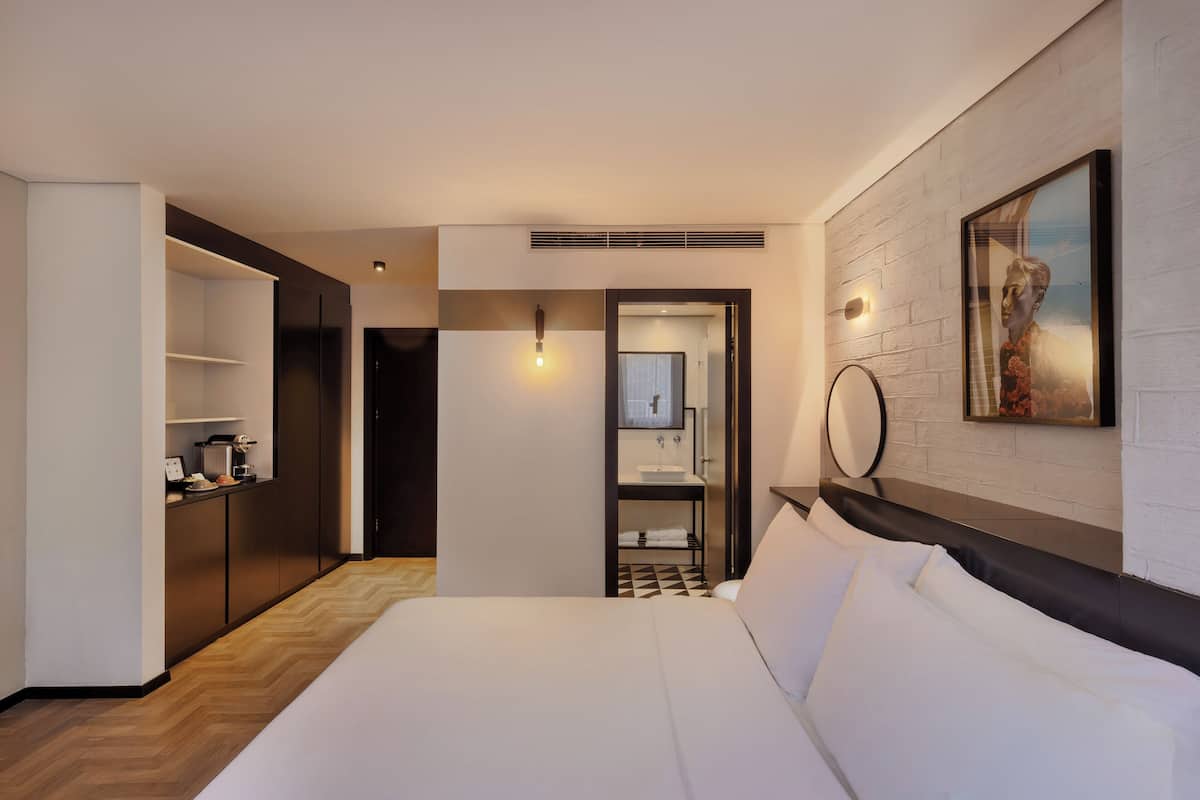 A hotel room with a large bed, a small kitchenette, a bathroom, and a view of the city.