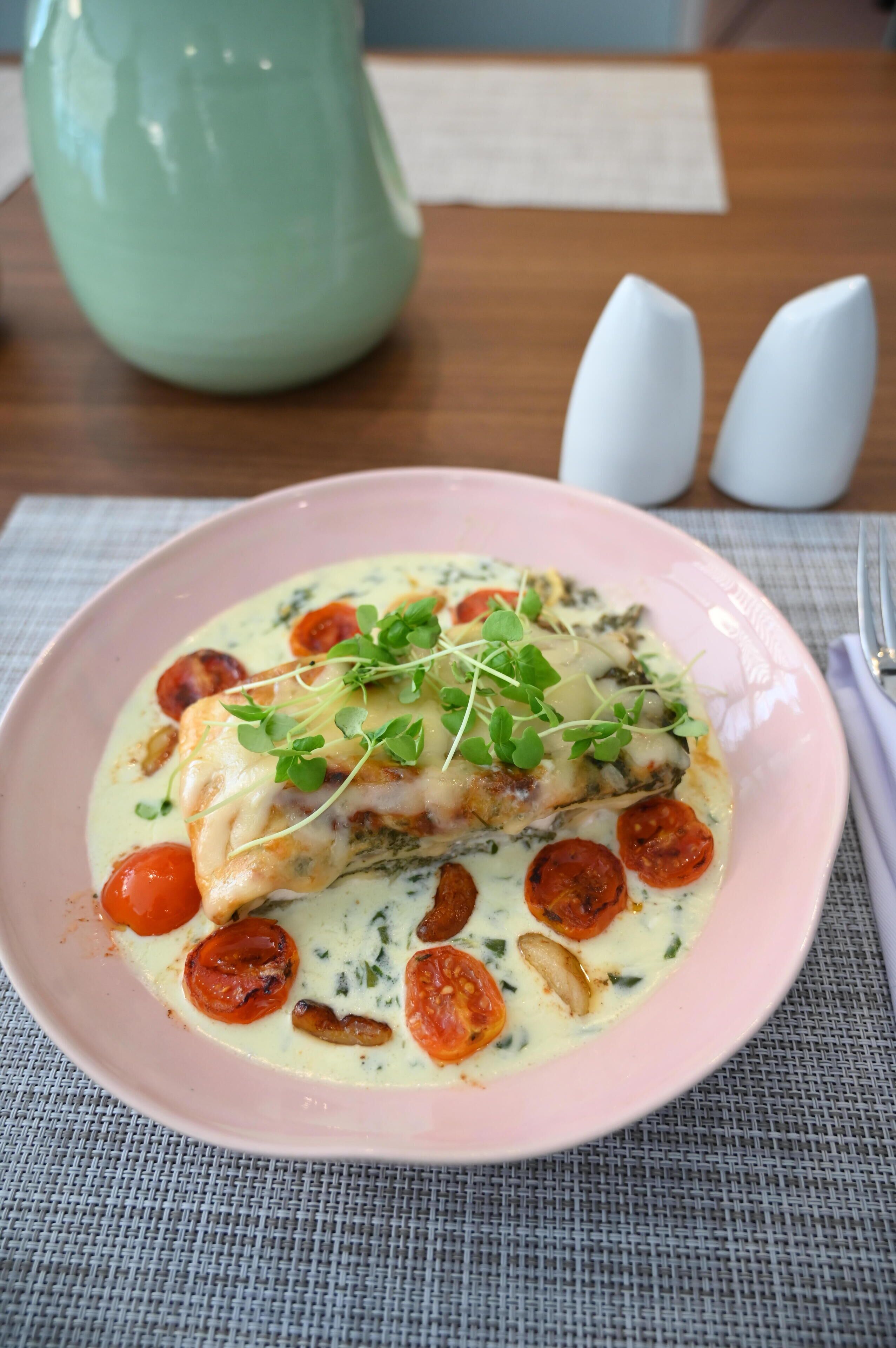 Un plato de comida con un trozo de pescado, tomates cherry y hojas verdes sobre un plato rosa.