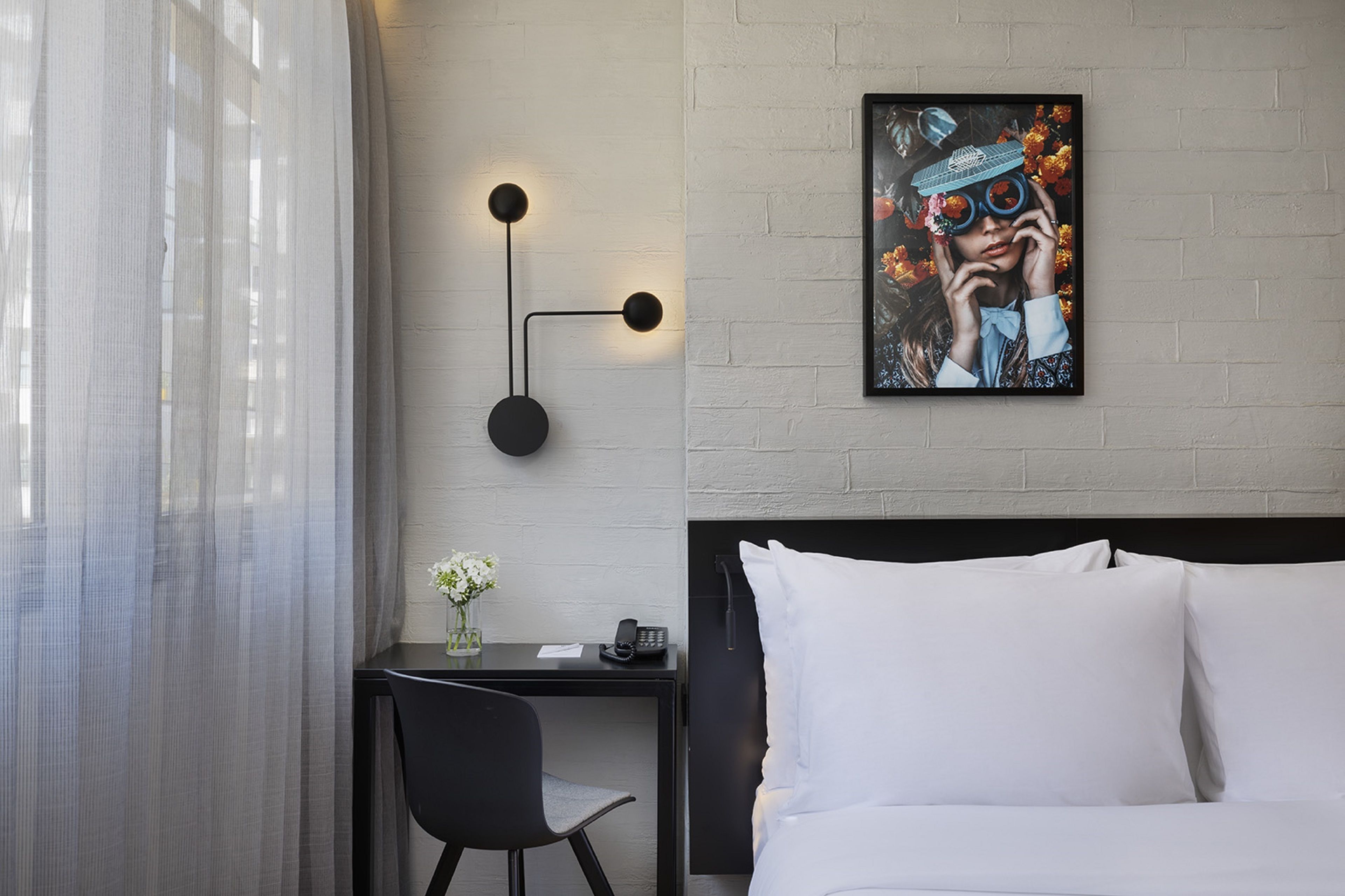 A hotel room with a bed, a desk with a chair, a phone, and a wall-mounted light fixture.