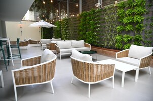 Un área de estar moderna al aire libre con mobiliario de mimbre y una pared verde con plantas.