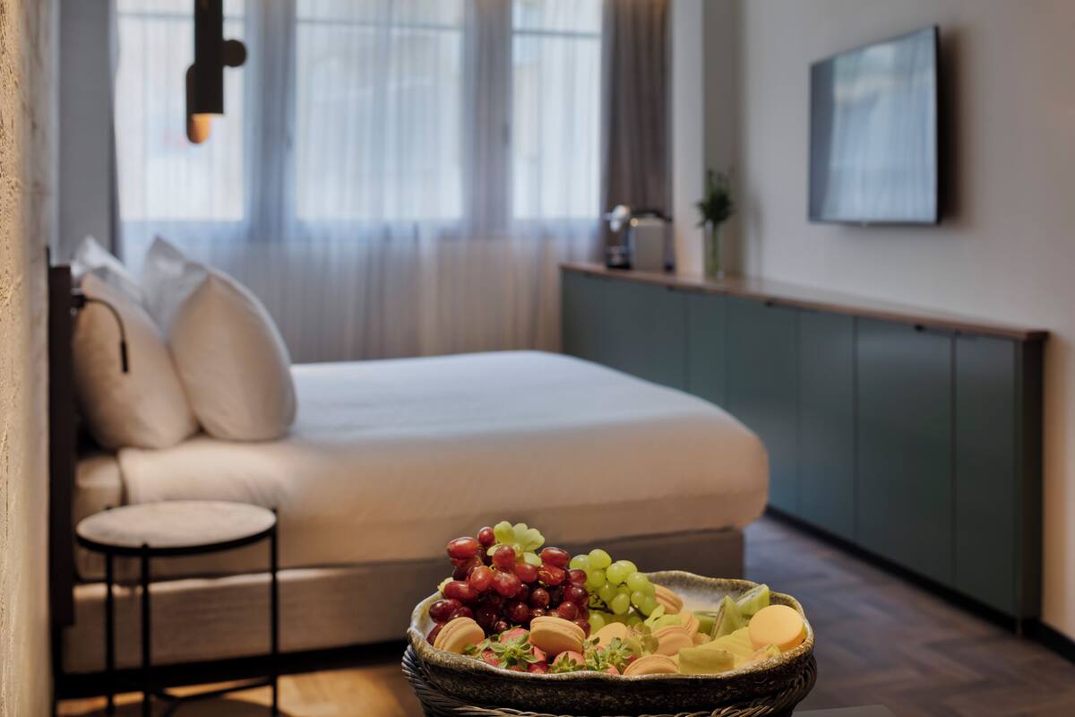 A bedroom with a bed, a small round table, and a wicker basket with snacks.