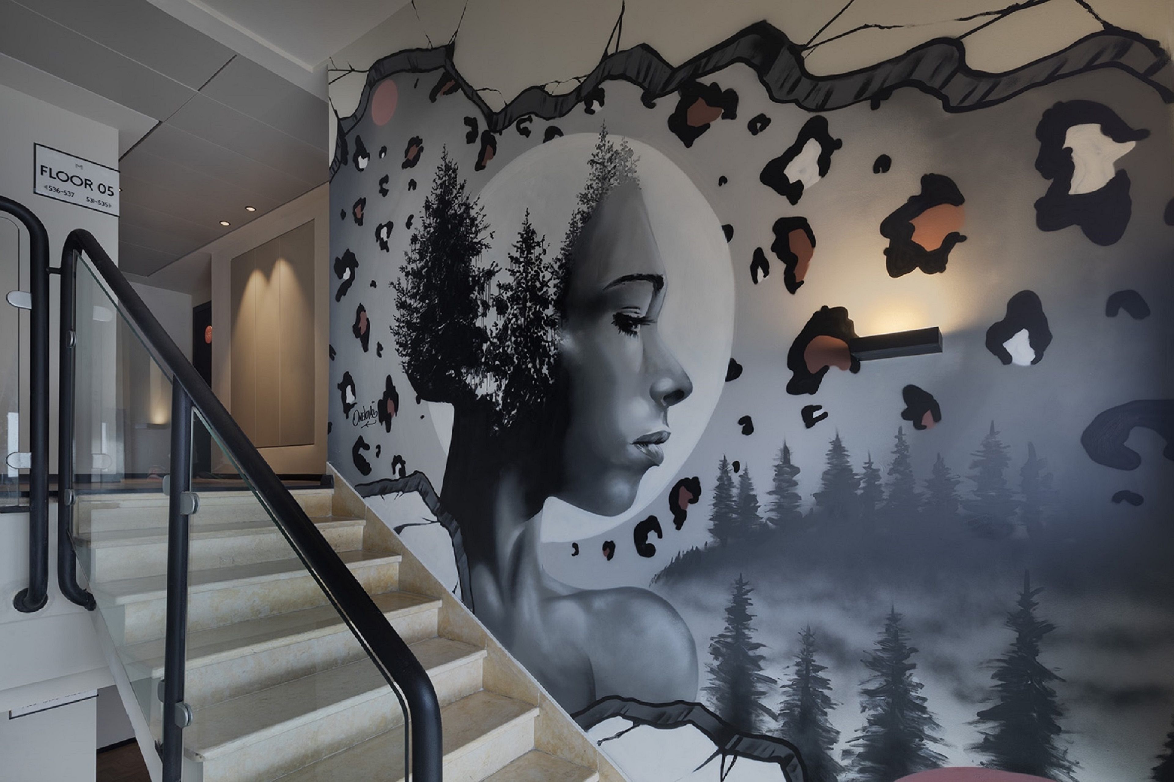Una escalera con un mural que muestra un paisaje forestal y el rostro de una mujer.