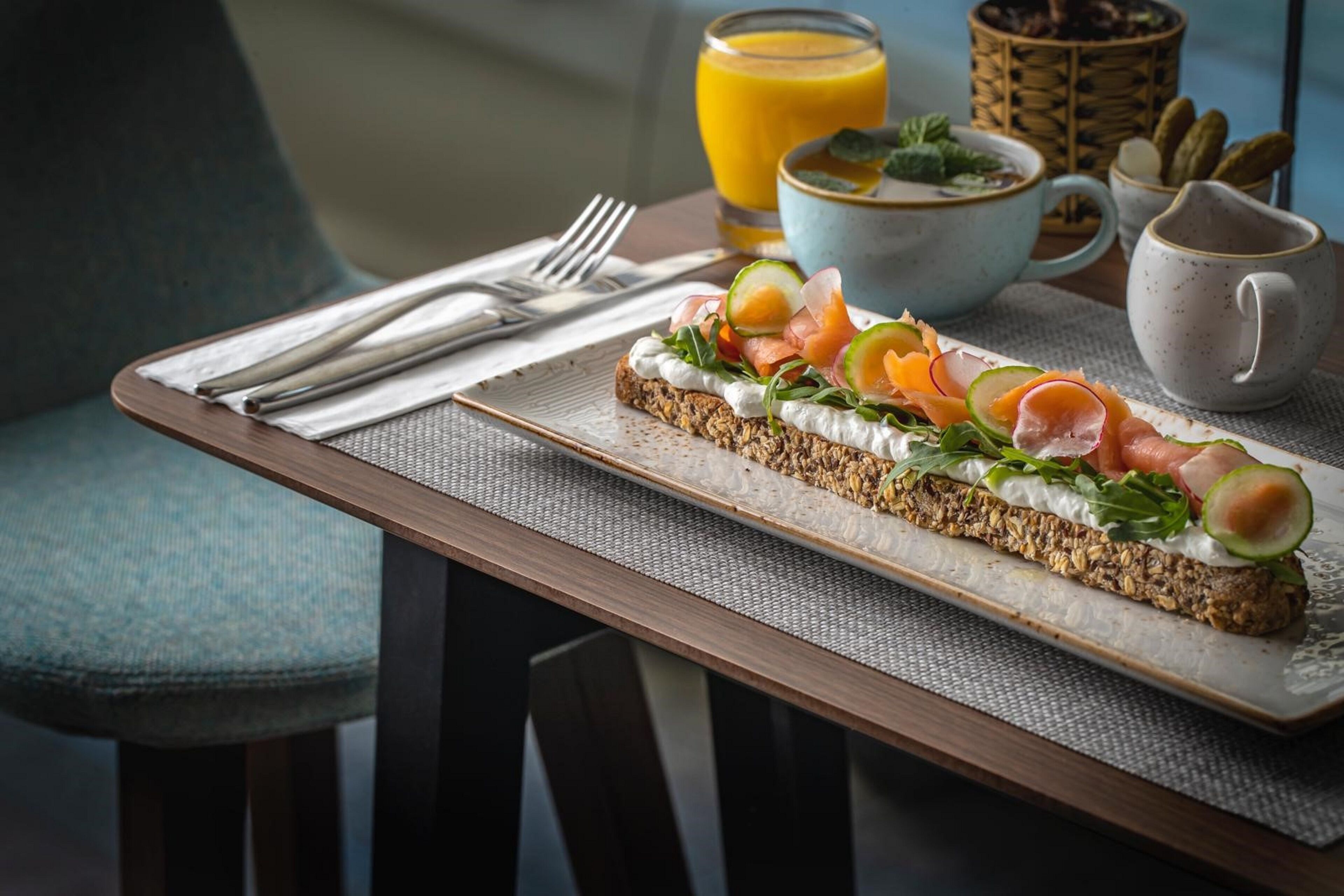 Una bandeja de desayuno con un sándwich, un vaso de zumo de naranja y un tazón de sopa sobre una mesa.